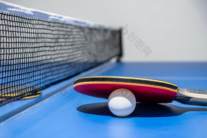 特写镜头红色的表格网球球拍和白色球的蓝色的平发出难闻的气味表格与黑色的网表格网球桨体育竞争设备室内活动和锻炼为概念背景特写镜头红色的表格网球桨白色球和网