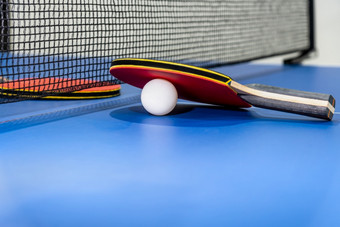 红色的表格网球球拍和白色球的蓝色的平发出难闻的气味表格与黑色的网两个表格网球桨体育竞争设备室内活动和锻炼为概念背景红色的表格网球桨白色球和网