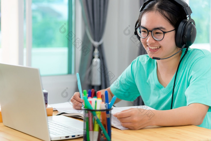 亚洲年轻的女人学生与眼镜耳机女孩研究快乐写作请注意书看视频会议移动PC电脑大学类在线互联网学习距离教育首页亚洲女人学生快乐类在线学习