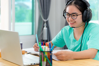 亚洲年轻的女人<strong>学生</strong>与眼镜耳机女孩研究快乐写作请注意书看<strong>视频</strong>会议移动PC电脑大学类在线互联网学习距离教育首页亚洲女人<strong>学生</strong>快乐类在线学习