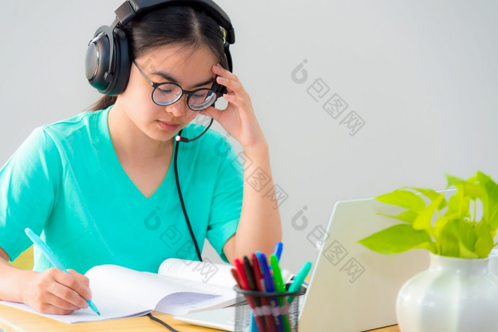 亚洲女人学生十几岁的女孩与眼镜耳机坐着看严重的阅读书担心使用移动PC电脑表格学习在线研究教育从类大学首页亚洲女人严重的阅读书学习在线