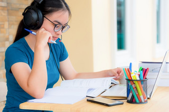 亚洲女人学生十几岁的女孩与眼镜耳机坐着看严重的阅读书担心使用移动PC电脑表格学习在线研究教育从类大学首页亚洲女人严重的阅读书学习在线