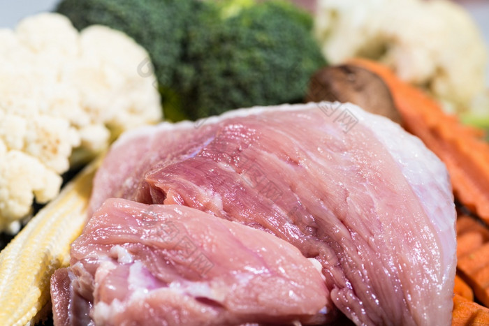 关闭一块新鲜的生肉猪肉和许多蔬菜是婴儿玉米西兰花花蘑菇胡萝卜菜花成分为食物准备烹饪肉猪肉和蔬菜为食物准备