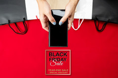 黑色的星期五出售女人手在线购物智能手机与购物袋红色的背景