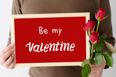 情人节一天概念男人。手持有红色的玫瑰和情人节词木框架站在白色背景
