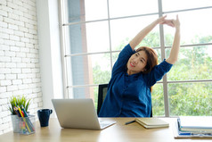 年轻的亚洲女人伸展运动身体为放松而工作与移动PC电脑她的桌子上首页办公室生活方式业务情况