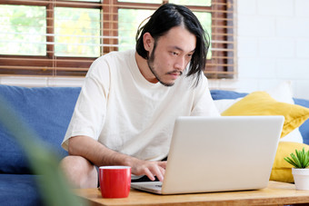 年轻的亚洲男人。休闲风格使用移动PC电脑生活房间首页背景人和技术生活方式工作首页
