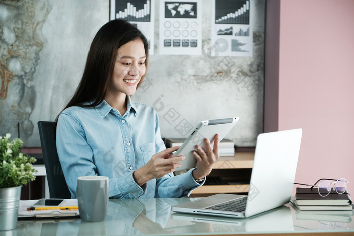 年轻的亚洲女商人使用平板电脑与微笑脸积极的情感办公室休闲办公室生活概念