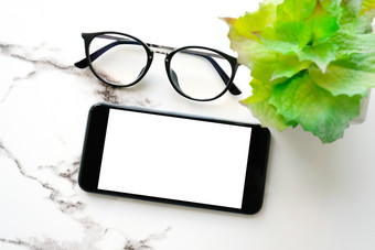 白色聪明的电话与空白屏幕和眼镜白色大理石表格背景为模拟模板技术和生活方式概念