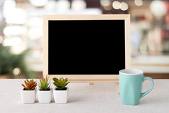 空白黑板和绿色咖啡杯站袋桌布在模糊餐厅与散景背景空间为文本模拟产品显示蒙太奇