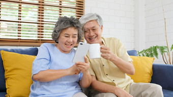 快乐高级亚洲夫妇使用聪明的电话而坐着沙发首页生活房间背景活跃的高级人退休和技术生活方式