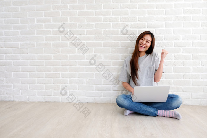 年轻的亚洲女人使用移动PC电脑坐着前面白色砖墙背景与复制空间人和技术生活方式教育业务概念