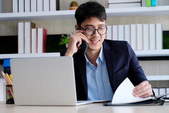 年轻的亚洲商人阅读论文会说话的电话办公室业务沟通和技术概念