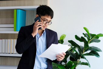 年轻的亚洲商人阅读<strong>论文</strong>会说话的电话办公室业务沟通和技术概念