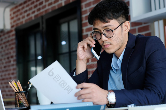 年轻的亚洲商人阅读论文会说话的电话办公室业务沟通和技术概念