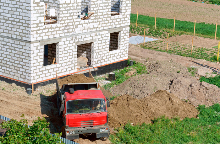 卡车和建筑使白色砖的自动倾卸车带来了沙子的建设网站转储卡车附近的房子下建设