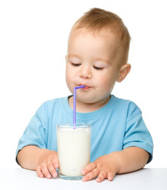可爱的小男孩喝牛奶使用稻草而坐着表格孤立的在白色