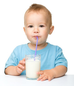 可爱的小男孩喝牛奶使用稻草而坐着表格孤立的在白色
