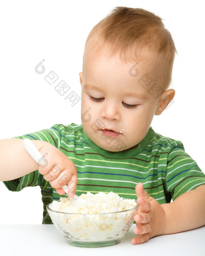 可爱的小男孩吃小屋奶酪使用勺子孤立的在白色
