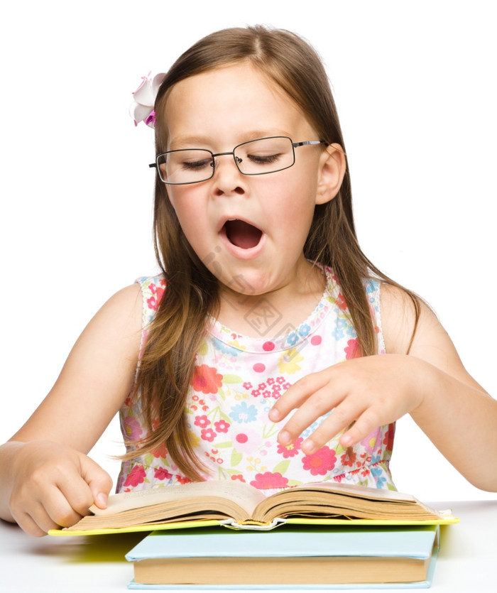 的小女孩打呵欠而阅读书而且穿眼镜孤立的在图片