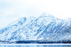 冬天湖与白雪覆盖的松树的银行的岩石山的阿尔泰山雾在的冬天湖