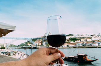 手持有玻璃红色的酒俯瞰码头贝拉和蓬特唐路易斯的河杜罗港口葡萄牙手持有玻璃红色的酒港口葡萄牙