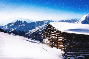 高高度木的小木屋小屋与光雪下降与阿尔卑斯山脉山范围背景高高度木的小木屋小屋与光雪下降的阿尔卑斯山脉
