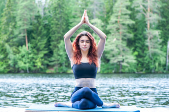 年轻的瑜珈女孩练习瑜伽坐着变异戈穆哈萨那牛脸的姿势的码头美丽的湖概念健康的生活和自然平衡