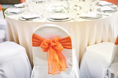 的婚礼接待晚餐表格与氨纶白色封面椅子与橙色透明硬纱腰带