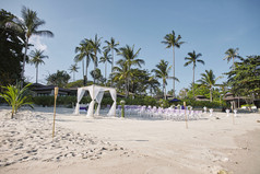 海滩婚礼聚会地点安排海边的白色沙子拱和坛装饰与白色软织物的竹子框架白色拉奥椅子安排棕榈树和椰子背景