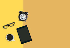 现代首页办公室工作场所概念黑色的报警时钟杯黑色的咖啡眼镜和平板电脑黄色的柔和的背景与复制空间