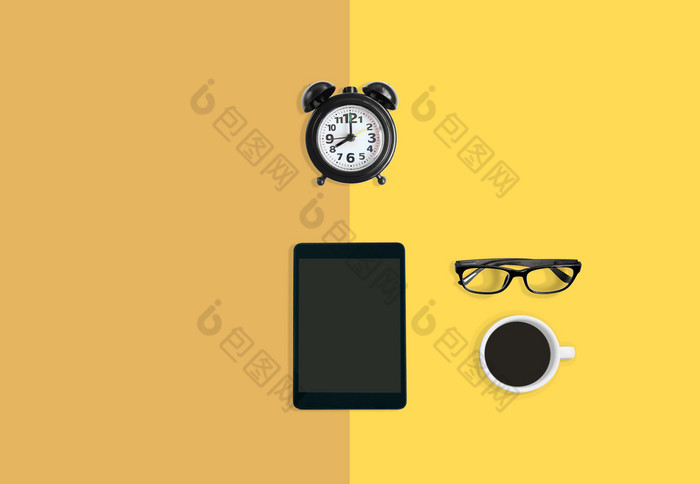 现代首页办公室工作空间概念黑色的报警时钟杯黑色的咖啡眼镜和平板电脑黄色的柔和的背景与复制空间