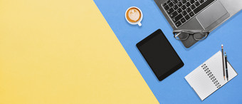 现代办公室桌面工作场所与移动PC平板电脑笔记本眼镜和杯热咖啡黄色的蓝色的纹理背景与复制空间平铺为横幅壁纸业务概念