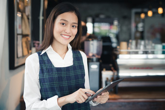 亚洲女人咖啡师微笑与平板电脑她的手女员工是采取订单从在线客户温暖的照片的咖啡商店