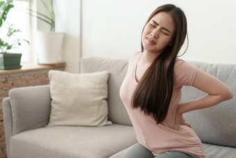 亚洲女孩有腰疼痛坐着沙发首页年轻的女孩有疼痛从的肌肉健康和疾病概念