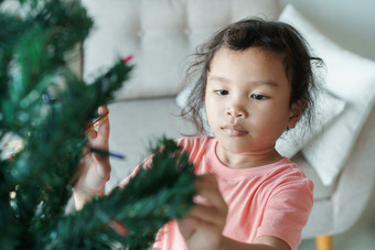 亚洲女孩是准备绿色圣诞节树为的假期季节她的首页的小女孩装修的圣诞节树