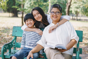 快乐亚洲家庭与妈妈。祖母和儿子坐着的板凳上而的妈妈。拥抱他们这两个的公园的概念生活方式家庭假期