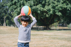 亚洲小男孩玩的草坪上与球的公园户外