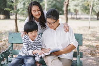 快乐亚洲家庭与妈妈。祖母和儿子坐着的板凳上而读书的公园的概念生活方式家庭假期