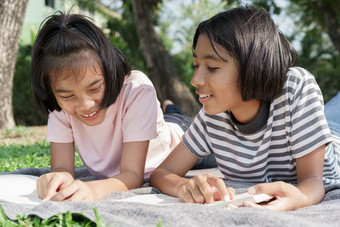 快乐亚洲学生而说谎读书的毯子的夏天亚洲两个女孩微笑和放松在一起公园的早....的女学生来了研究场旅行和学会了户外