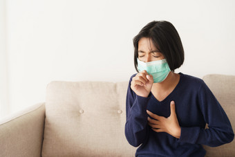 亚洲女孩症状咳嗽和是保护与医疗面具而坐着沙发亚洲孩子穿保护面具疫情流感新冠病毒生活房间首页健康和疾病概念