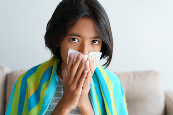 亚洲女孩有流感季节和打喷嚏使用纸组织而坐着的生活房间首页特写镜头的孩子的脸健康和疾病概念