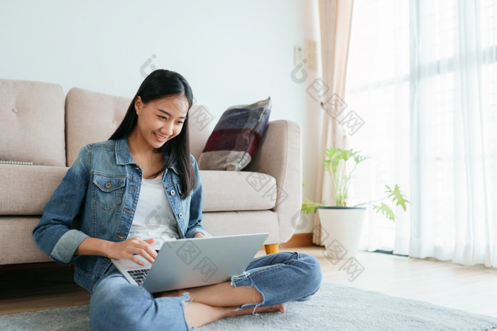 亚洲女孩穿牛仔裤使用移动PC而坐着的地板上首页自由女孩是视频会议与的同事们社会媒体概念工作从首页和新正常的