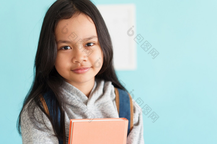 快乐亚洲小女孩微笑的脸亚洲孩子持有书和背包而站室内首页肖像孩子看相机概念背包学校