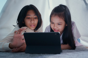 快乐两个女孩亚洲使用平板电脑帐篷晚上亚洲孩子拥抱娃娃说话学习的数字电脑首页