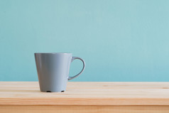 咖啡杯子的地方棕色（的）木桌子上和蓝色的壁纸变形背景与复制空间
