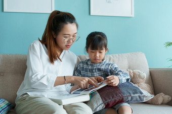 亚洲家庭与妈妈。和女儿阅读书在一起而坐着的沙发的生活房间首页早....