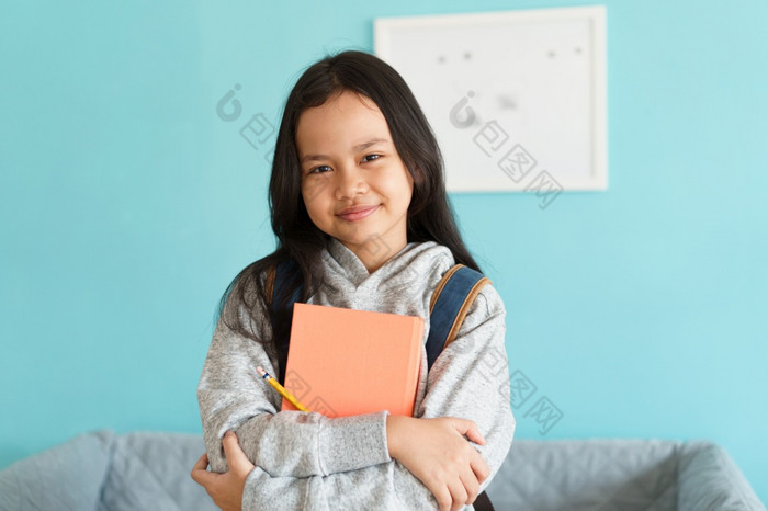 快乐亚洲小女孩微笑的脸亚洲孩子持有书和背包而站室内首页肖像孩子看相机概念背包学校