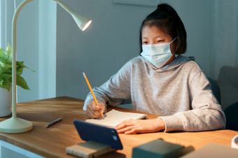 亚洲女孩做家庭作业在线学习与聪明的电话晚上亚洲女人穿保护面具疫情流感新冠病毒首页健康和疾病概念