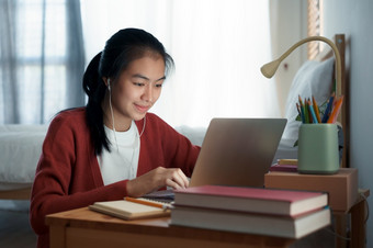 亚洲女人视频调用在线通过的互联网导师电脑移动PC与耳机亚洲女孩研究而坐着的卧室晚上概念在线学习首页